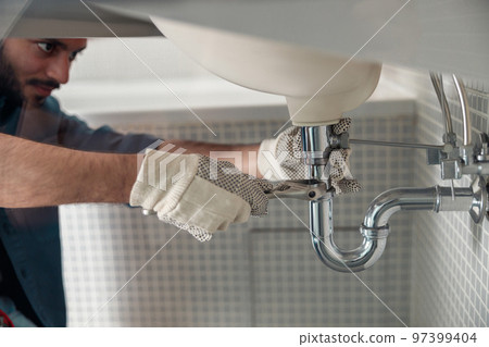 Close up of indian plumber is repairing faucet of a sink at bathroom using adjustable wrench Close up of indian plumber is repairing faucet of a sink at bathroom using adjustable wrench 97399404