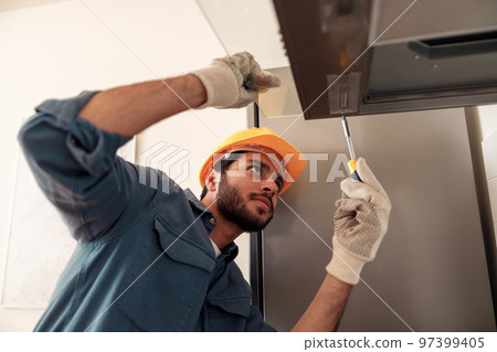 Handyman in uniform repairing kitchen extractor, replacing filter in cooker hood.Maintenance concept Handyman in uniform repairing kitchen extractor, replacing filter in cooker hood.Maintenance concept 97399405