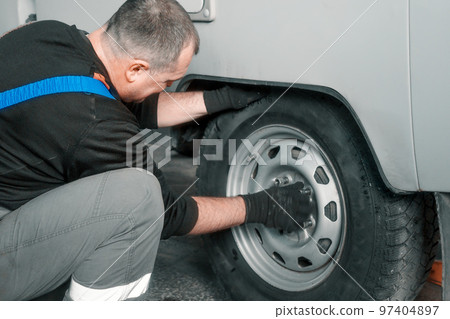 Man changes wheel of car in car service. Professional auto mechanic in overalls removes wheel from 97404897