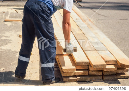 Work at sawmill on summer day. Timber harvesting for construction. Carpenter stacks boards Work at sawmill on summer day. Timber harvesting for construction. Carpenter stacks boards 97404898
