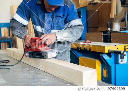 Carpenter in work clothes processes wood with grinder. Polishing of wood surface. Middle-aged man 97404899