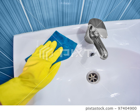 Hand in yellow rubber glove with rag wipes white sink. Cleaning and disinfection with cleaning agent 97404900