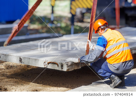 Slinger lays concrete slab on construction site on summer day. Worker in protective vest and Slinger lays concrete slab on construction site on summer day. Worker in protective vest and 97404914