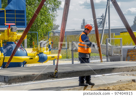 Slinger lays concrete slab on construction site on summer day. Worker in protective vest and 97404915