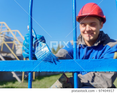 Professional painter in clothing and helmet paints metal fence or fence made of reinforcement with 97404917