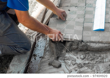 Bricklayer lays tiles on cement. Photo of hand with tile close-up. Authentic workflow. Construction 97404920