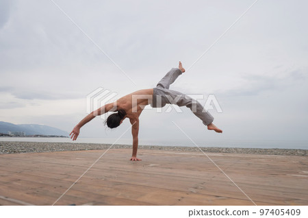 Shirtless caucasian man doing backflip on pebble beach.  97405409