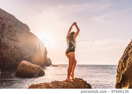 Young woman with long hair in black swimsuit and boho style braclets practicing outdoors on yoga mat by the sea on a sunset. Women's yoga fitness routine. Healthy lifestyle, harmony and meditation Young woman with long hair in black swimsuit and boho style braclets practicing outdoors on yoga mat by the sea on a sunset. Women's yoga fitness routine. Healthy lifestyle, harmony and meditation 97406236