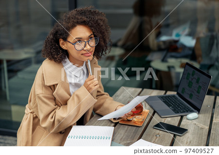 Focused Afro american woman freelancer working remotely while sitting on cafe terrace Focused Afro american woman freelancer working remotely while sitting on cafe terrace 97409527