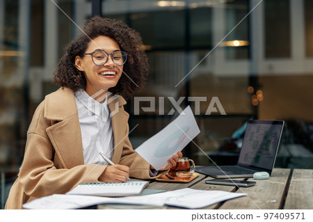 Happy Afro american woman freelancer working remotely while sitting on cafe terrace 97409571