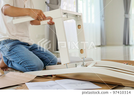 Man assembling white chair furniture at home Man assembling white chair furniture at home 97410314