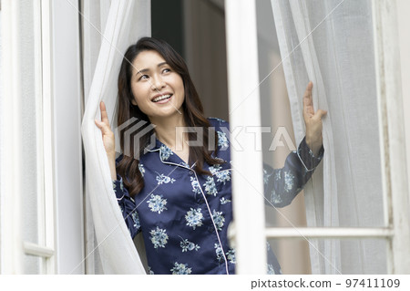 Arafif woman in pajamas looking out the window image of waking up 97411109