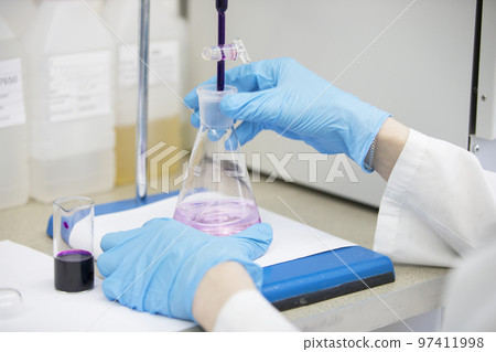 The hands of a technician in blue rubber gloves are holding a flask. Pharmaceutical industry. Chemical laboratory 97411998