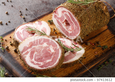 Sliced salted-cured bacon roll in spices and herbs close-up on a kitchen board. Horizontal Sliced salted-cured bacon roll in spices and herbs close-up on a kitchen board. Horizontal 97413612