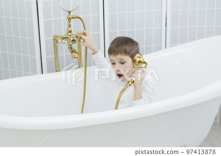 Baby in the bathroom in clothes.The boy sits in the bath and plays the phone.Talking on the phone Baby in the bathroom in clothes.The boy sits in the bath and plays the phone.Talking on the phone 97413878
