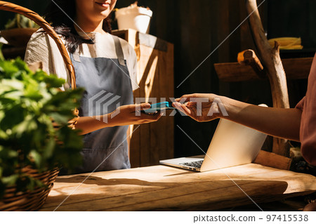 Vendor receiving payment from customer by card machine. Hands of unrecognizable women standing at a counter in an outdoor market and making a transaction. 97415538
