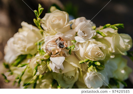 A pair of gold wedding rings on a brown background, in the background a bouquet with white flowers A pair of gold wedding rings on a brown background, in the background a bouquet with white flowers 97420585