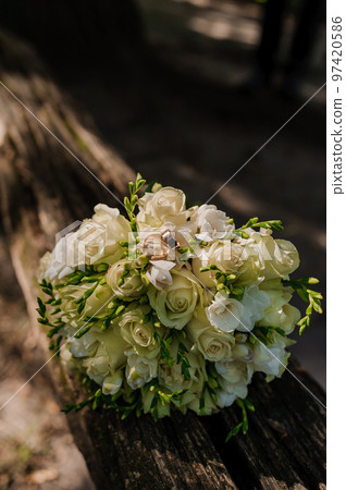 A pair of gold wedding rings on a brown background, in the background a bouquet with white flowers A pair of gold wedding rings on a brown background, in the background a bouquet with white flowers 97420586