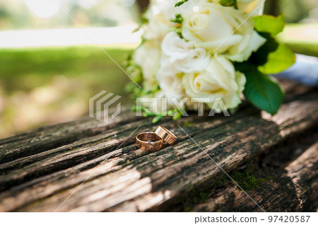A pair of gold wedding rings on a brown background, in the background a bouquet with white flowers A pair of gold wedding rings on a brown background, in the background a bouquet with white flowers 97420587