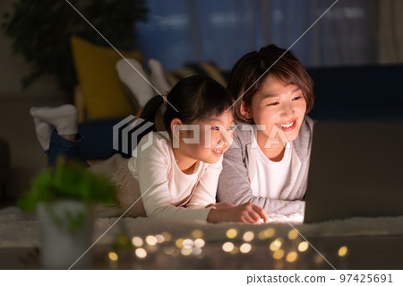 Elementary school girl and mom lying in the living room at night and looking at a computer 97425691