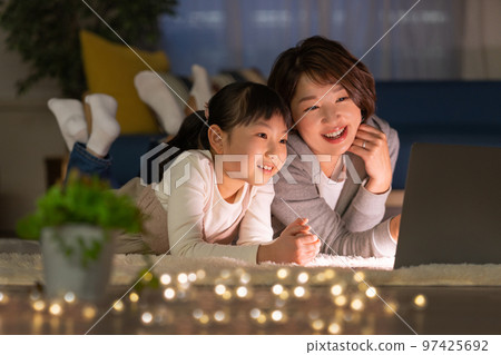 Elementary school girl and mom lying in the living room at night and looking at a computer 97425692