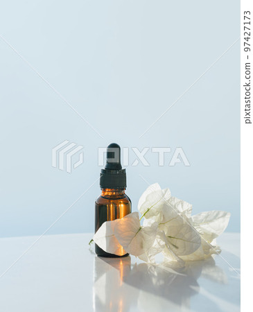 Natural medicine or essential aroma oil or beauty essence amber glass vial with dropper exotic white flowers and airy pale blue background. Face and body spa serum care concept Natural medicine or essential aroma oil or beauty essence amber glass vial with dropper exotic white flowers and airy pale blue background. Face and body spa serum care concept 97427173