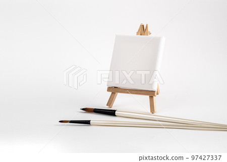 Mini easel with white blank canvas, paint brushes. Art concept Mini easel with white blank canvas, paint brushes. Art concept 97427337
