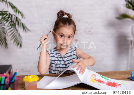 Inspired little girl at the table draw with paints Inspired little girl at the table draw with paints 97428418
