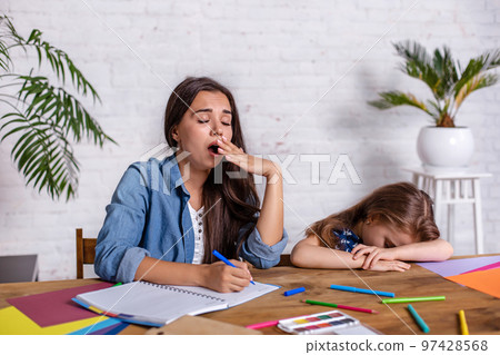 Cute little girl sleeping while her mother looking tired, helping her with studying. 97428568