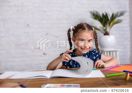 Inspired little girl at the table draw with crayons or do home work Inspired little girl at the table draw with crayons or do home work 97428616