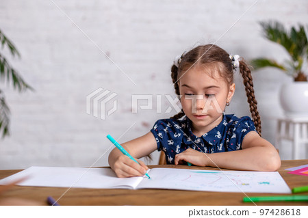 Inspired little girl at the table draw with crayons or do home work Inspired little girl at the table draw with crayons or do home work 97428618