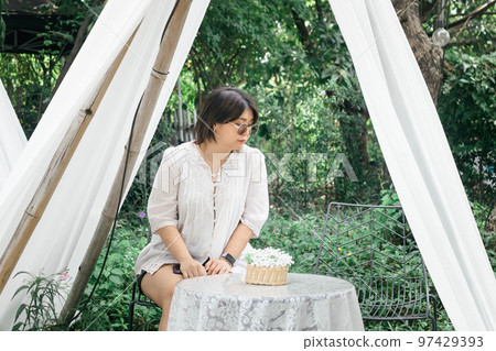 A young attractive Asian woman sitting on the chair at the garden backyard. A young attractive Asian woman sitting on the chair at the garden backyard. 97429393