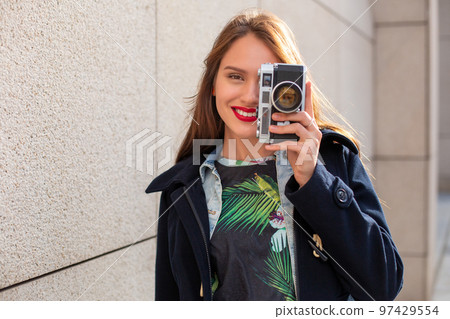 Happy hipster girl making photo with retro camera on city street 97429554