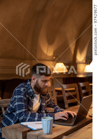 Young professional surfing the Internet on his laptop in a cafe Young professional surfing the Internet on his laptop in a cafe 97429677