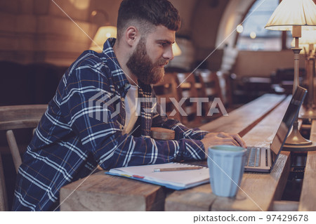 Young professional surfing the Internet on his laptop in a cafe Young professional surfing the Internet on his laptop in a cafe 97429678