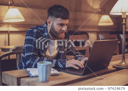 Young professional surfing the Internet on his laptop in a cafe Young professional surfing the Internet on his laptop in a cafe 97429679