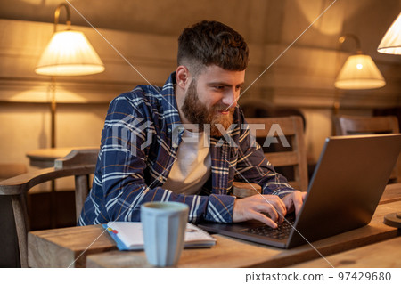 Young professional surfing the Internet on his laptop in a cafe Young professional surfing the Internet on his laptop in a cafe 97429680