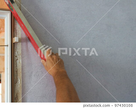 working with a level to check the desired angle during repairs in the room, a man's hand holds a red level and measures the slope of the door frame to the wall when mounting the leaf working with a level to check the desired angle during repairs in the room, a man's hand holds a red level and measures the slope of the door frame to the wall when mounting the leaf 97430108