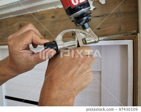 regulation of the flow of silicone foam in the nozzle of the construction gun in male hands when installing the door frame and filling the gap with mounting foam regulation of the flow of silicone foam in the nozzle of the construction gun in male hands when installing the door frame and filling the gap with mounting foam 97430109