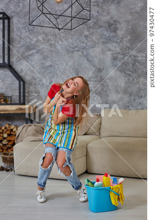 Happy young cleaning woman in apron with mop rejoicing in living room. Perfect order 97430477