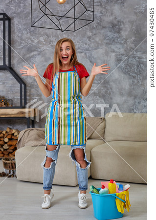 Happy young cleaning woman in apron with mop rejoicing in living room. Perfect order 97430485