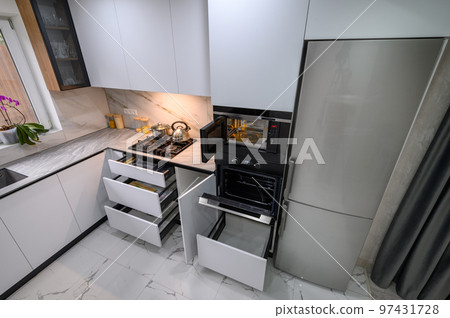 A spacious and updated kitchen with a white color scheme, a marble floor, an open ovens door, and pull-out shelves 97431728