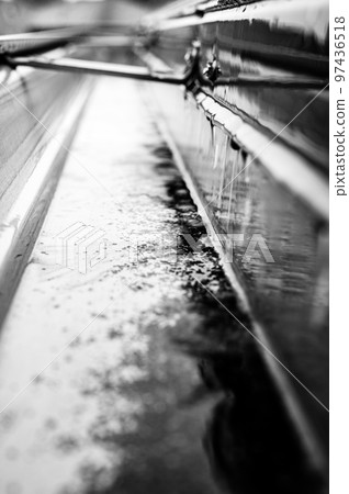 Selective focus on a section of residential guttering with hanger conveying water during a storm. Rain splatters and drops visible. 97436518