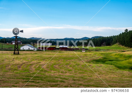 Rural homestead farmhouse in South Dakota with a windmill and hayfield.  97436638