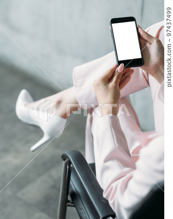Digital mockup. Office woman. Mobile technology. Elegant confident business lady holding smartphone blank screen sitting chair in light room interior. Digital mockup. Office woman. Mobile technology. Elegant confident business lady holding smartphone blank screen sitting chair in light room interior. 97437499