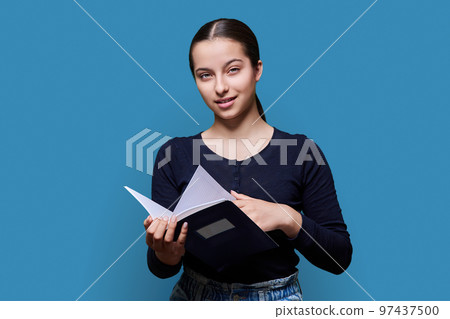 Teenager female student with notebook looking at camera on blue background 97437500