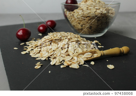 oatmeal on a black tray stand and a cup of glass bowl next to cherry berries. Roller food avtrak. Homemade cooking oatmeal on a black tray stand and a cup of glass bowl next to cherry berries. Roller food avtrak. Homemade cooking 97438008