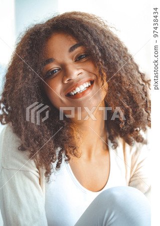 Happy relaxed African American ethnicity girl with closed eyes sitting on windowsill at home 97438434