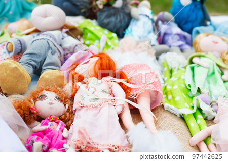 Defocus collection of handmade textile cloth baby boy and girl dolls in cute little sets of clothes standing on a festival market shelf. Closeup dolls. Out of focus Defocus collection of handmade textile cloth baby boy and girl dolls in cute little sets of clothes standing on a festival market shelf. Closeup dolls. Out of focus 97442625