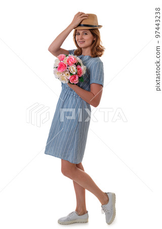 Full size portrait of an attractive young woman in summer dress and straw hat holding bouquet isolated over white background 97443238